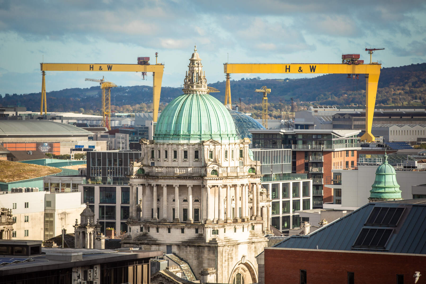 Belfast cityscape photo with Belfast City Hall featured and surrounding buildings and two cranes in the background
