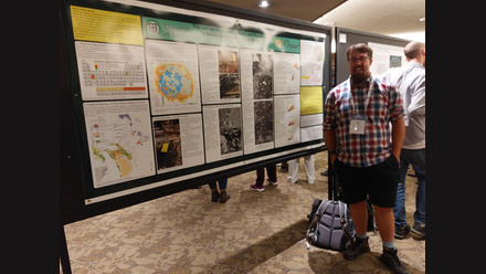 Man on the right hand of the image standing in front of a poster at a caonference