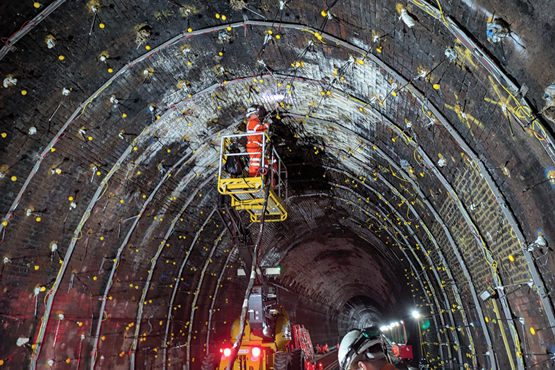 Construction worker applying geobear reinforcement to the interior of a rail tunnel