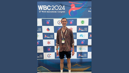 A man in a brown shirt and black shorts with white socks standing infront of a banner with visible text WBC 2024 aand logos beneath