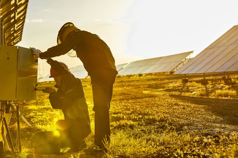 two electricians working at a junction box in a solar farm in a field