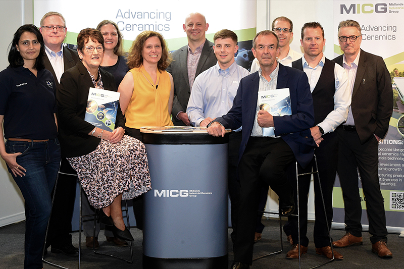 A group of men and women standing against a banner promoting the Midlands Industrial Ceramics Group