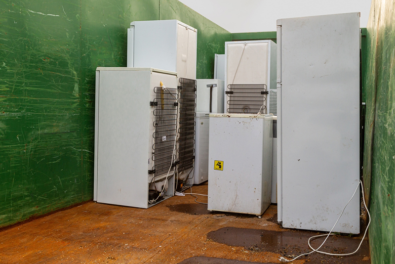 Old, worn-out tall refrigerators placed inside a large green container