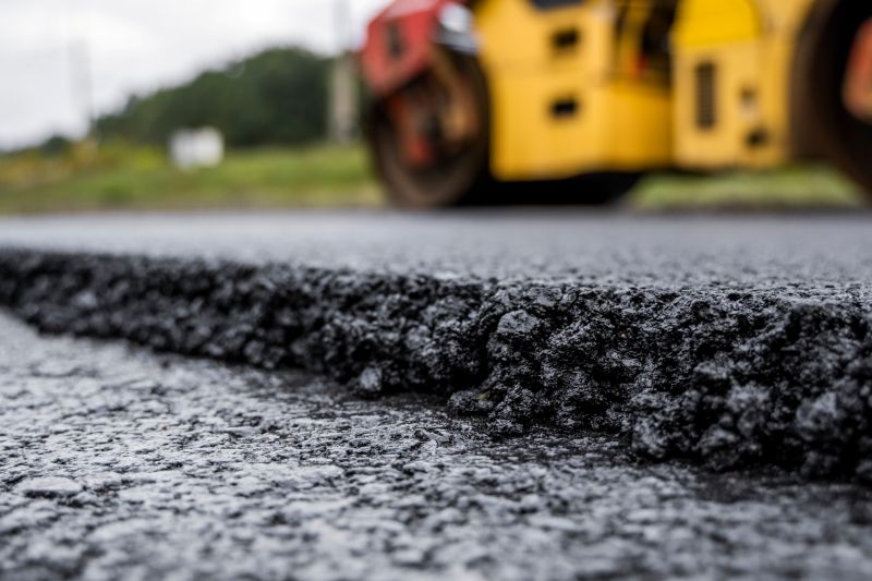 Asphalt road roller with heavy vibration roller compactor press new hot asphalt on the roadway on a road construction site pictured.