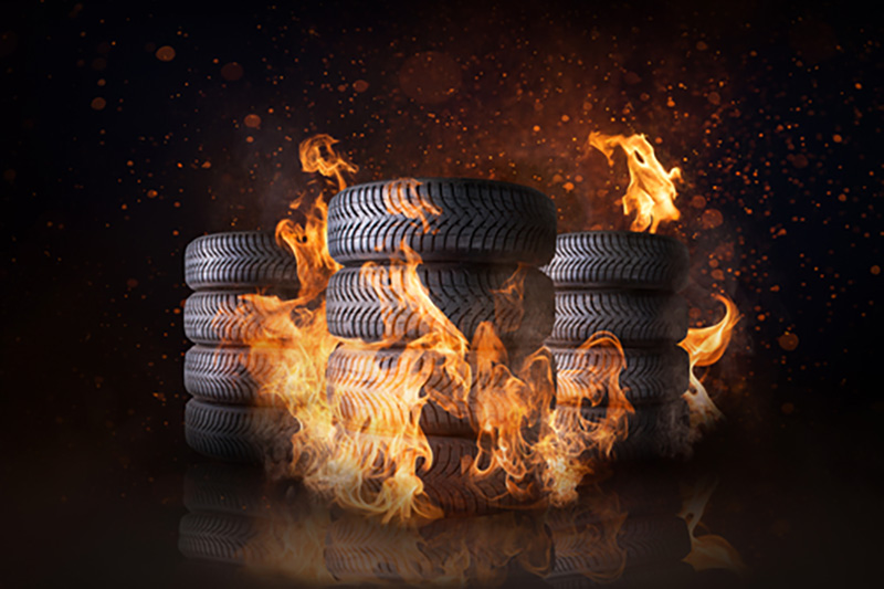 three stacks of tyres against a dark background with flames licking up the tyre stacks