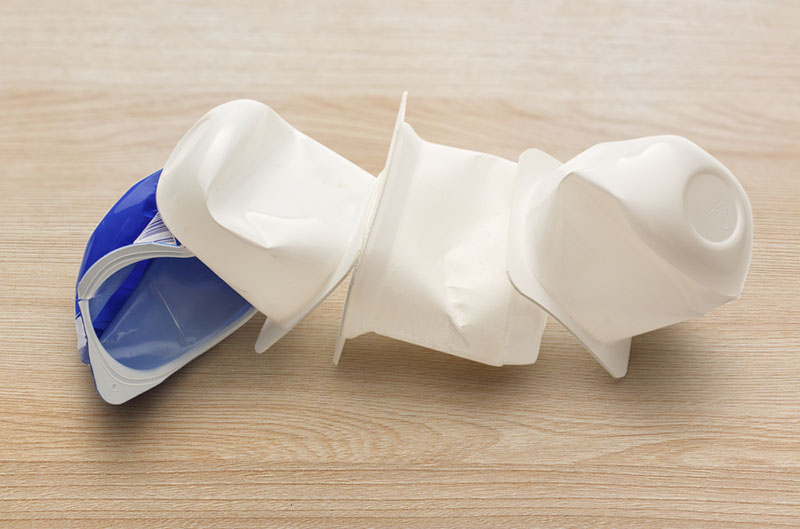 Empty crushed plastic yogurt pots on wooden background