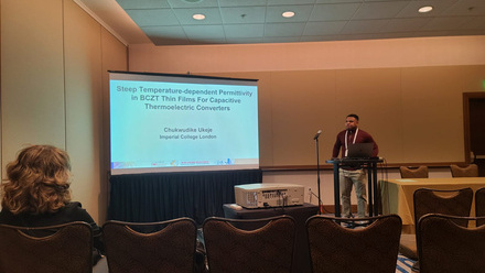 Large screen to the left with a man speaking to the right, lights are dimmed