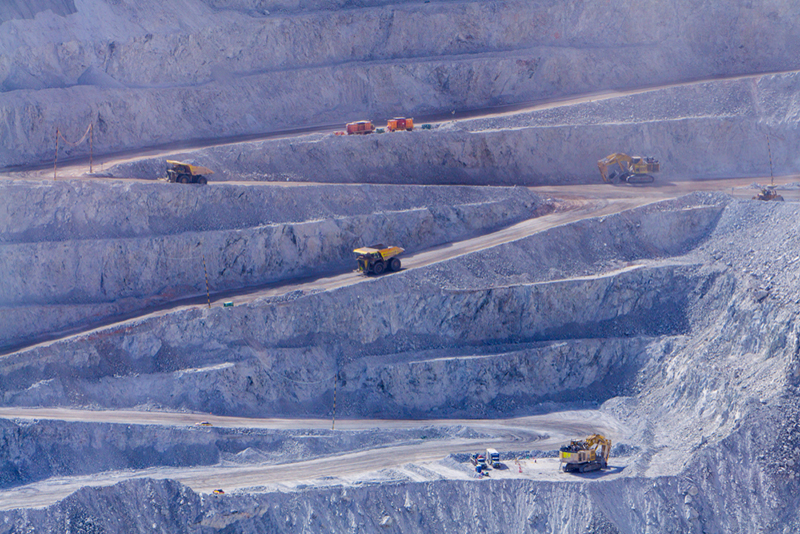 Huge mining trucks and diggers look tiny on the zig-zag steep roads on the side of a giant quarry