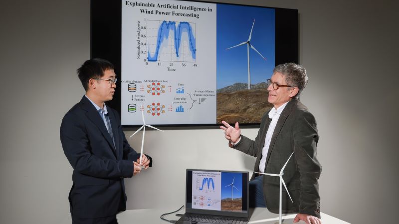 two men with models of wind turbines talking to each other in front of a presentation screen
