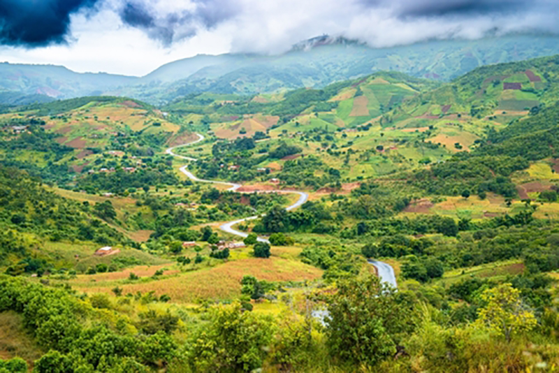 A picture from the sky of lush green countryside of Malawi, with hills in the background and a winding road going into the distance