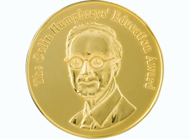 gold circular medal with raise letterin around the top edge reading The Colin Humpreys' Education Award, centred is an image of Humphreys with glasses