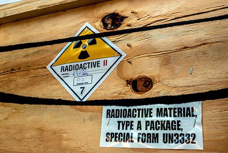 Two stickers on the side of a wooden box, one with the radioactive symbol and another sticker saying radioactive material