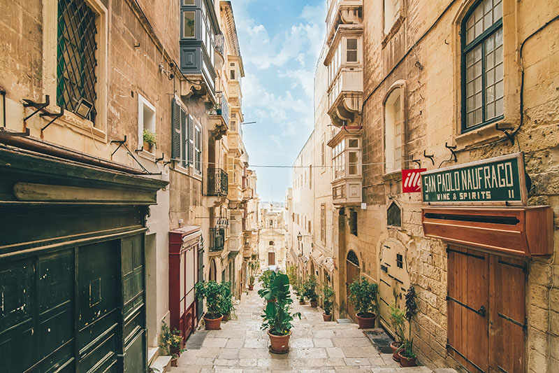 narrow padestrian street with bildings each site, plant pots are in the centre and along the sides, there is a red sign for coffee