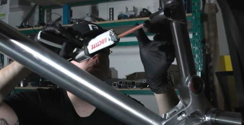 Man in a dark tee shirt and black gloves uses Loctite glue on a bike frame