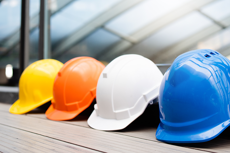 stock image of four hard hats - yellow, orange, white, blue - lined up in a row
