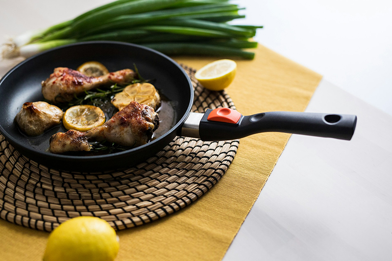 non-stick frying pan containing chicken drumsticks with a lemon and spring onions to the sides