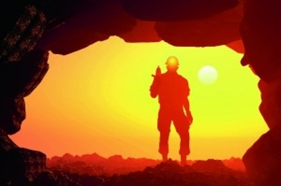 A cave like opening showing a yellow glow with the sillouette of a miner standing to the right