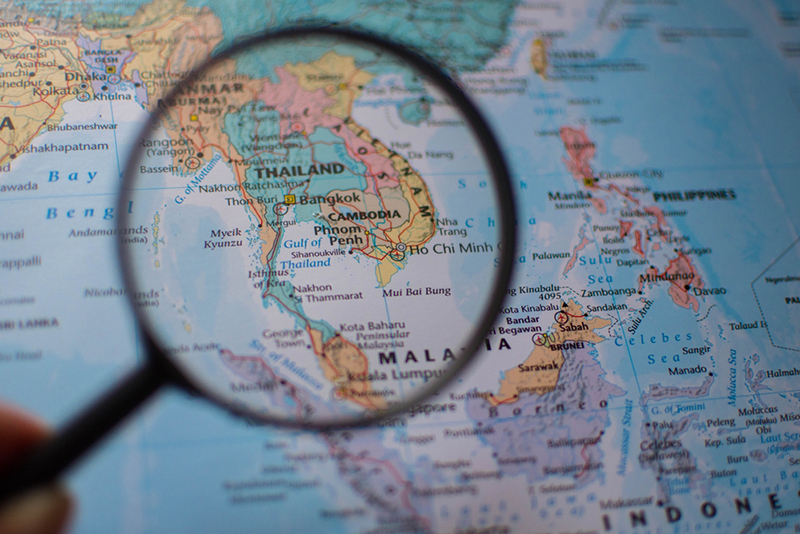 A magnifying glass highlights Southeast Asia, focusing on Thailand, Cambodia, and Vietnam