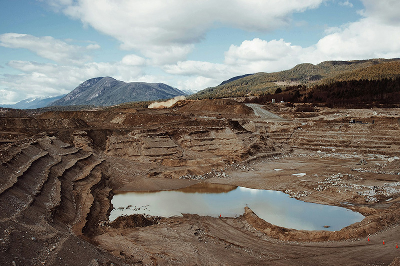 An open pit mine with water collected at the bottom under a cloudy sky