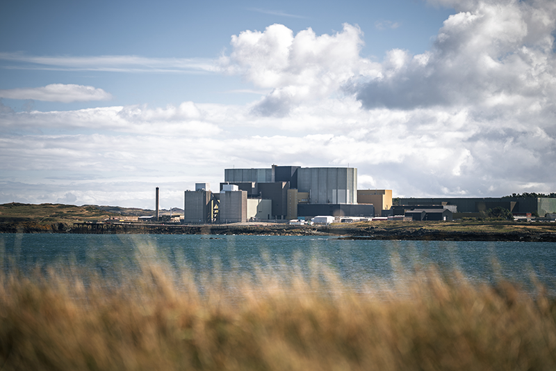 Stock image of the Wylfa nuclear power station in Wales, behind some grass and sea