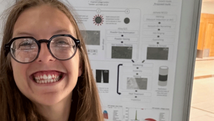 smiling female with glasses in front of a poster presentation