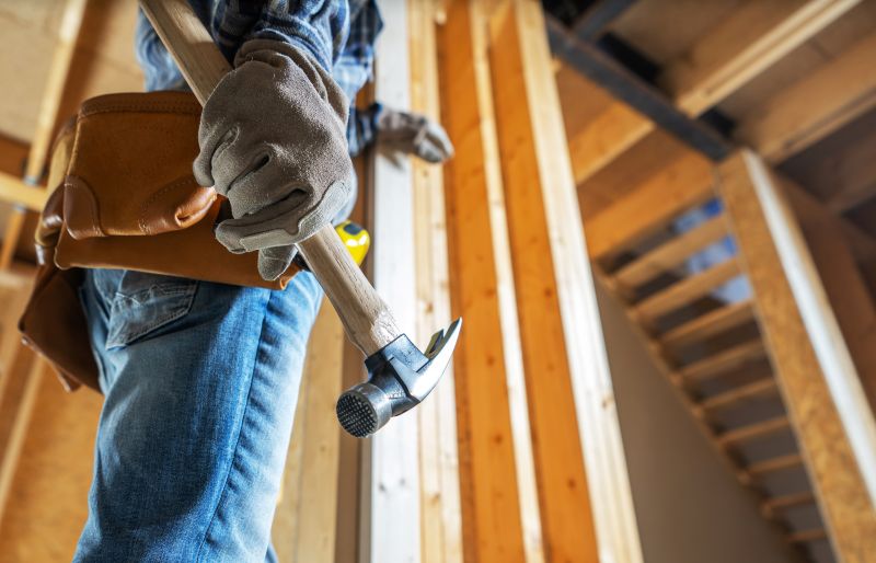 A construction worker grips a hammer and prepares to work on interior framing in a newly built home, shows the framing details and tools in use, pictured