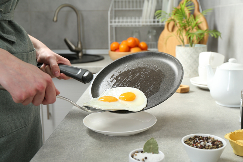 Woman putting fried eggs onto plate from frying pan in kitchen, closeup