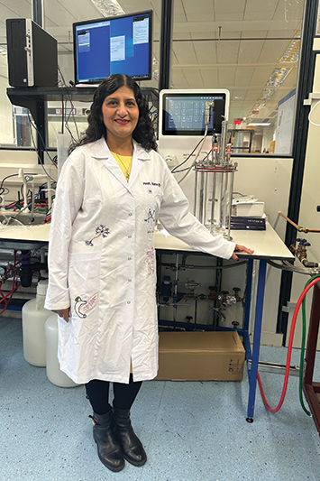 Professor Ipsita Roy, standing in a lab set-up wearing a lab coat embroidered with biology imagery