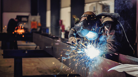shutterstock_613560062-Industrial Welder With Torch and Protective Helmet in big hall welding metal profiles.jpg