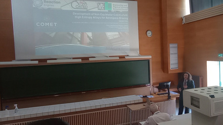 Man in suit in the right background giving a presentation on a wall screen