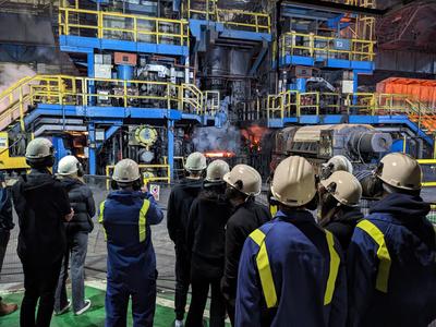 Group of people in hard hats and uniform look at steelmaking quipment