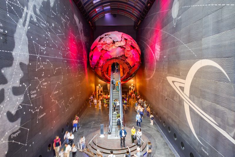 Visitors at the Natural History Museum travel use stairs to access a model of a planet