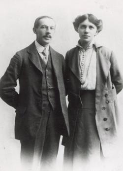 Man on the left with a moustache, woman to the right with a necklace and long coat