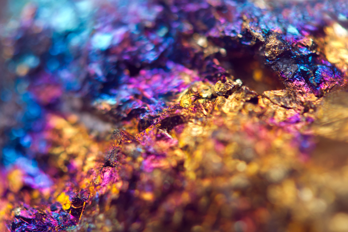 Macrophotograph of mineral containing gold, copper and iron ores in the form of gold, blue and purple crystals