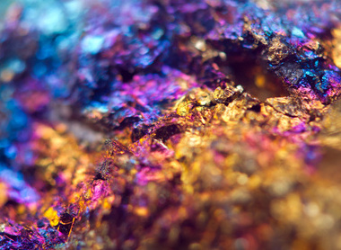 Macrophotograph of mineral containing gold, copper and iron ores in the form of gold, blue and purple crystals