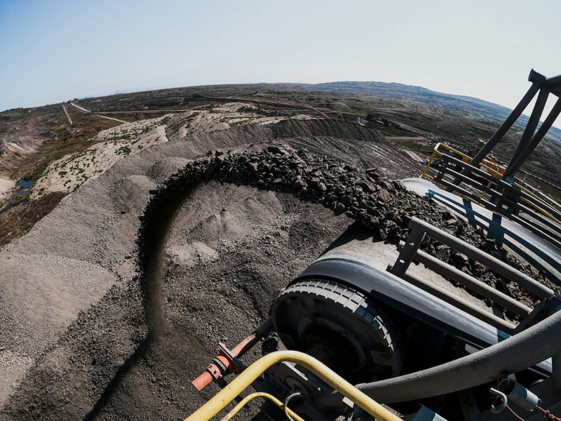a pile of coal with an extractor to the right which is spitting out lumps of coal
