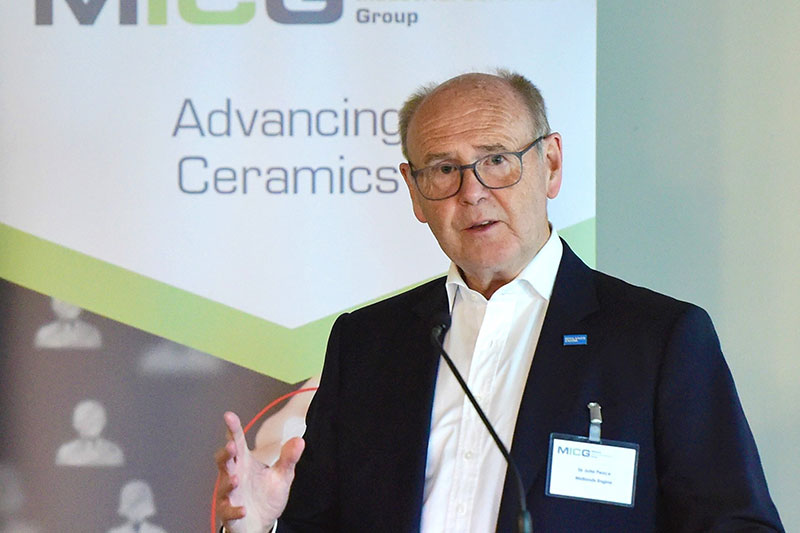 man with glasses in front of an advancing ceramics backdrop