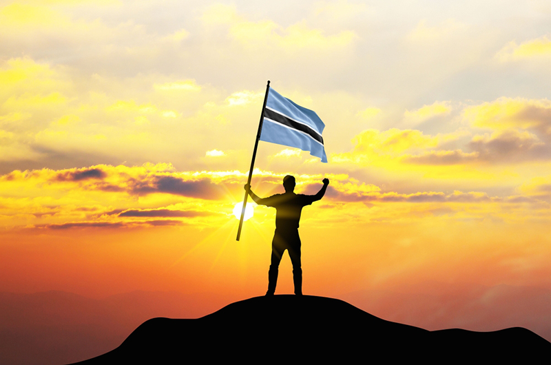 Botswana flag being waved by a man celebrating success at the top of a mountain against sunset or sunrise