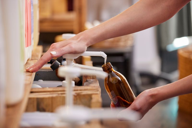Close up of woman refilling glass bottle with liquid soap in sustainable zero waste plastic free store