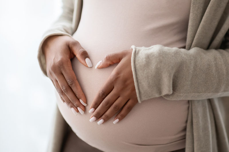 Pregnant black woman holding palms in heart shape on her big tummy