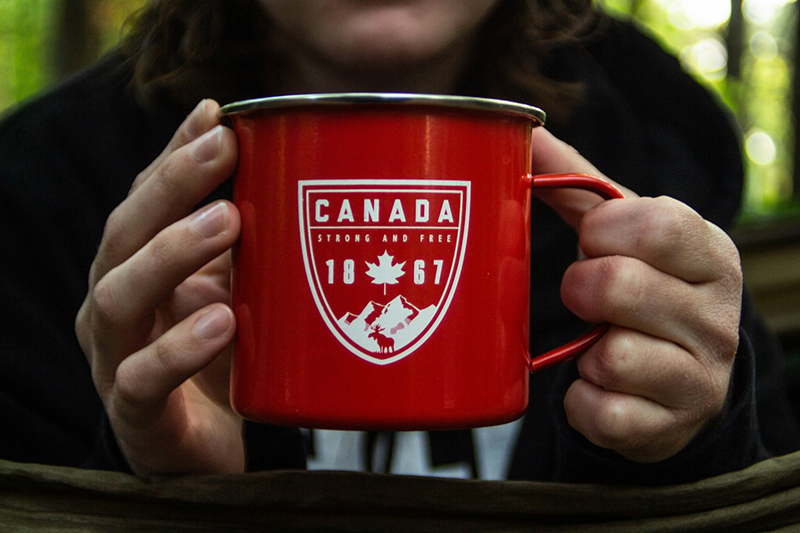 Person holds a red enamelled mug with Canadian maple leaf and slogan