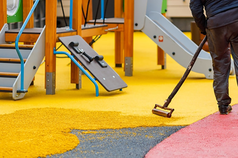 Someone rolling a rubber coating surface on the ground of a kids playpark