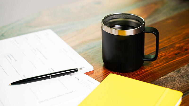 paperwork on a wooden table with a black ceramic mug