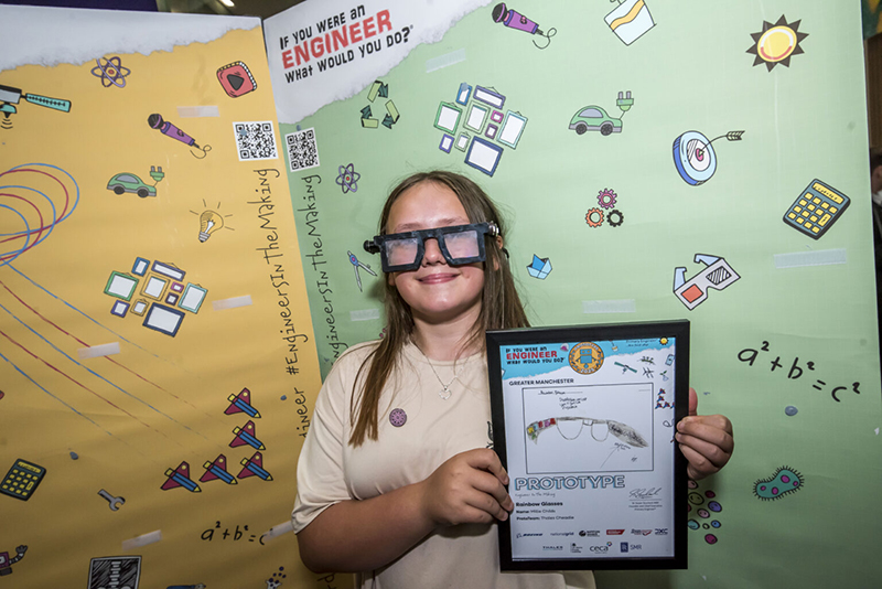 School girl Millie Childs wearing the prototype Rainbow Glasses against a green post promoting the Primary Engineer scheme