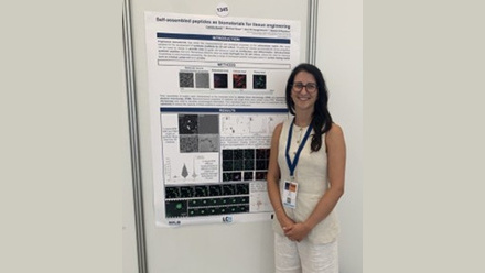 Young student dressed in white posing in front of a conference poster