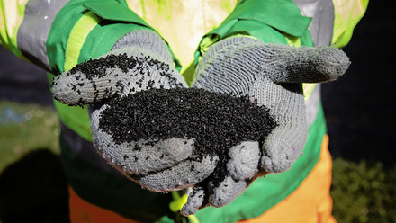 Close up of gloved hands holding a black powder.  The person is wearing safety clothing. 