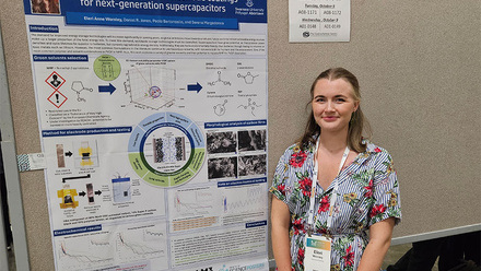 Poster presentation board with a female in a patterened dress and tied back hair standing to the right
