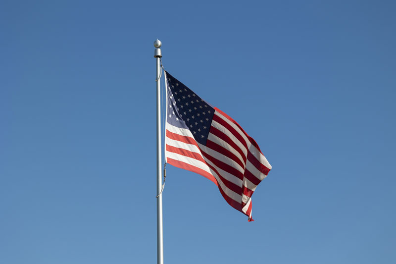 US flag flies from a silver coloured pole against a clear blue sy