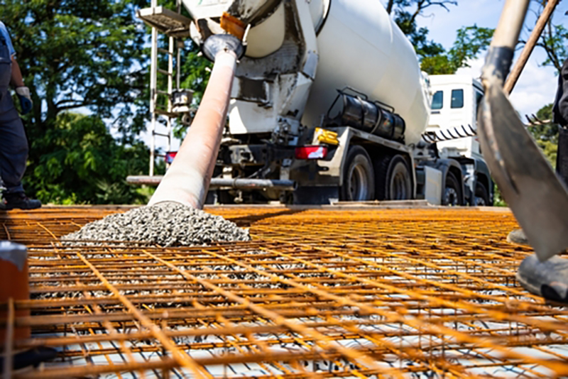 Concrete being poured from a concrete mixing truck directly onto a metal grid floor at a construction site