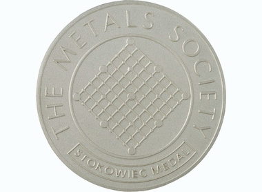 silver boardered medal with top outer reading the metals society, boxed at the bottom text reads Stokoweic medal, centre shows a metal lattice